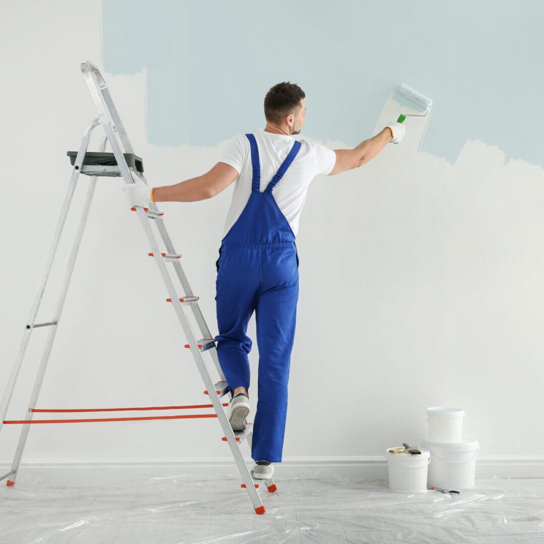 Man painting wall with light blue dye indoors, back view Painter on ladder applying paint to wall.