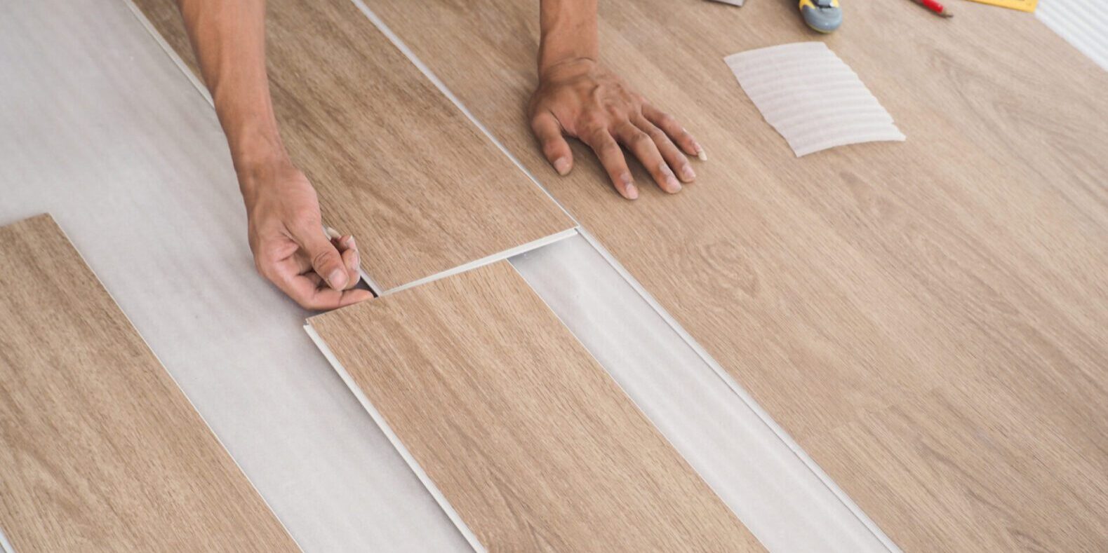 A technician is cutting luxury vinyl floor tiles with a cutter to lay the floor before placing it on the leveling foam. Person installing wooden flooring panels.